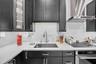 Dark finish cabinetry with glass-front accents, solid-surface countertops, stainless steel undermount sink, gooseneck faucet, and integrated stainless