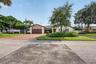 Single-story residence featuring a tile roof, brick-paver driveway, attached multi-car garage, and established landscaping