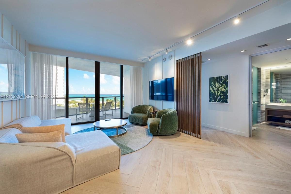 Herringbone-patterned wood-finish flooring, floor-to-ceiling glass sliding doors, slatted wood partition, and adjustable track lighting