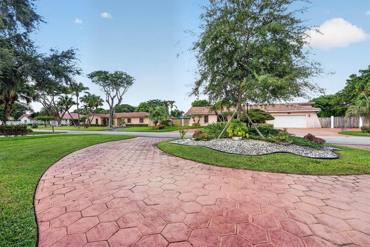 Curved hexagonal paver driveway, manicured lawn, stone-accented landscaping, and attached garage