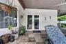 Covered patio featuring multi-tonal stone flooring, white textured exterior wall, dual-pane glass French doors, and a wood-finish ceiling with an inte