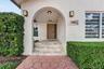 Covered entryway featuring a stone-stepped porch, arched architectural detail, square-paneled front door, and metal wall-mounted light fixtures