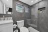 Bathroom featuring large-format dark stone wall tile, glass-enclosed shower with built-in recessed niche, stone-topped vanity with metallic faucet, an