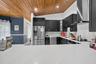 Kitchen featuring vaulted wood-paneled ceiling, white stone-finish countertops, stainless steel appliances, dark wood cabinetry with built-in wine sto