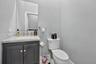 Dark-finished vanity with stone-surface countertop, rectangular undermount sink, brushed-metal faucet, and frameless wall-mounted mirror