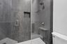Walk-in shower featuring floor-to-ceiling stone-finish tile, frameless glass door, built-in wall niche, brushed metallic fixtures, and a stationary sh