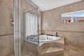Bathroom featuring natural stone tile wall and floor surfaces, a raised corner jetted soaking tub, and a glass-enclosed shower with chrome fixtures