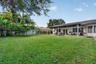Expansive backyard featuring a manicured lawn, mature trees, a perimeter privacy fence, and a covered patio with a tile roof