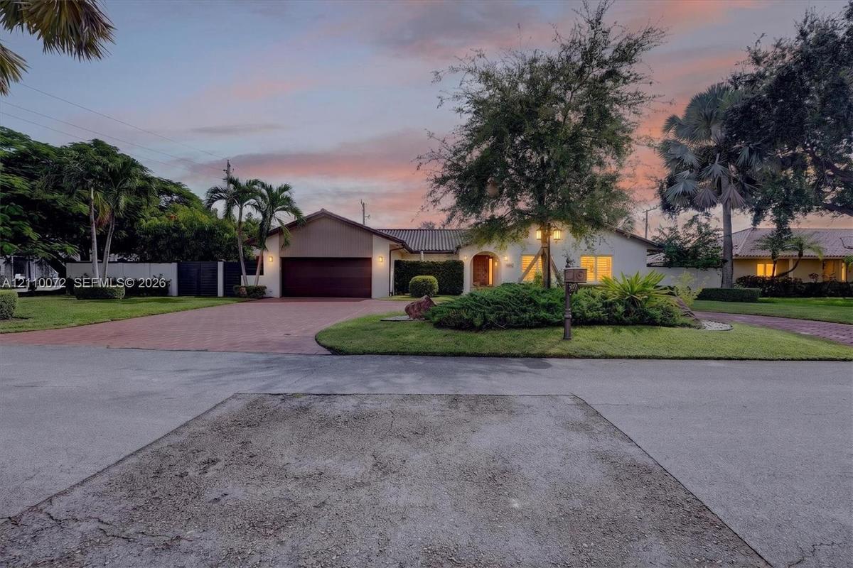 Single-story residence featuring a tile roof, an attached garage with a finished door, a paved driveway, and mature landscaping