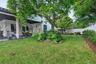 Covered concrete patio featuring structural columns, expansive lawn, stone-bordered landscaping, and perimeter privacy wall