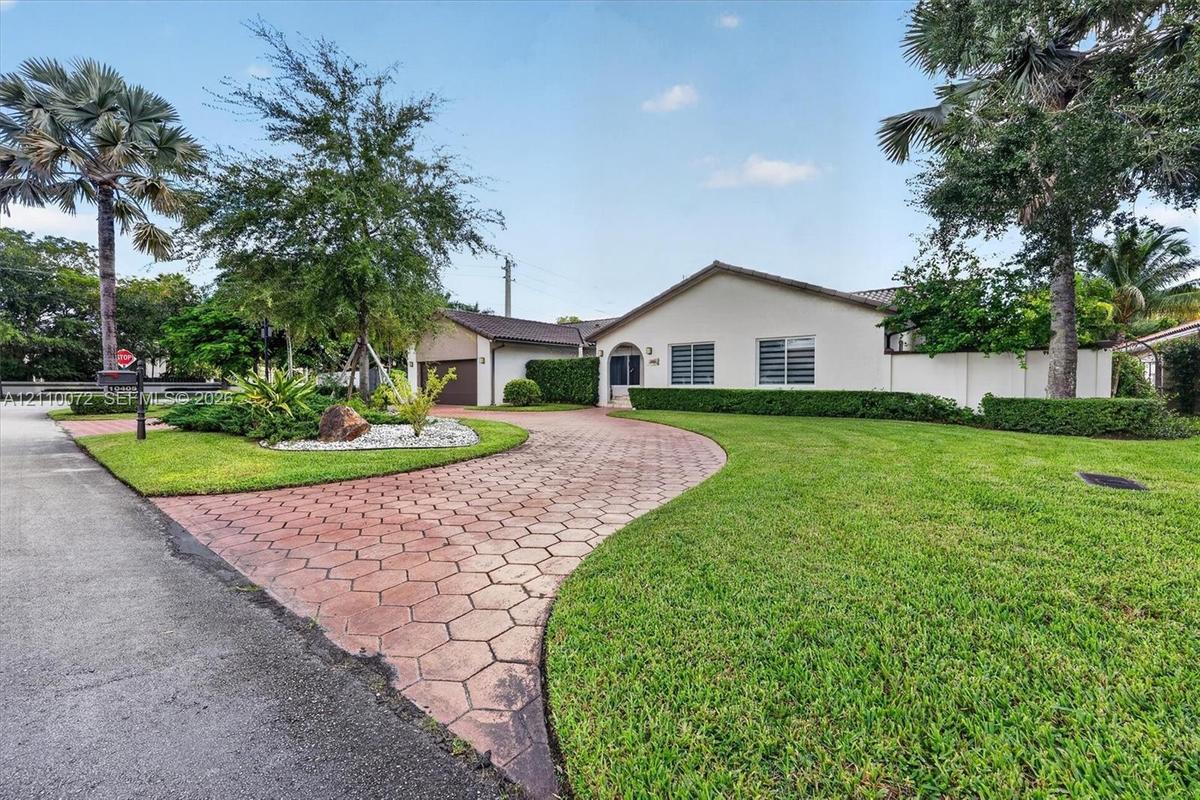 Exterior featuring a stucco facade, a geometric paver driveway, mature palm trees, manicured landscaping, and a multi-car garage
