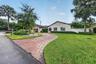 Exterior featuring a stucco facade, a geometric paver driveway, mature palm trees, manicured landscaping, and a multi-car garage