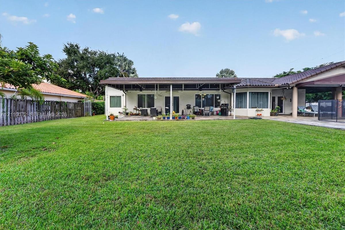 Expansive backyard featuring a manicured lawn, full-width covered patio, tile roof, and privacy fencing