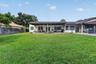 Expansive backyard featuring a manicured lawn, full-width covered patio, tile roof, and privacy fencing