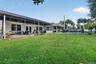 Backyard featuring an expansive lawn, stone-paved patio, covered terrace, in-ground swimming pool with safety fencing, and mature palm trees