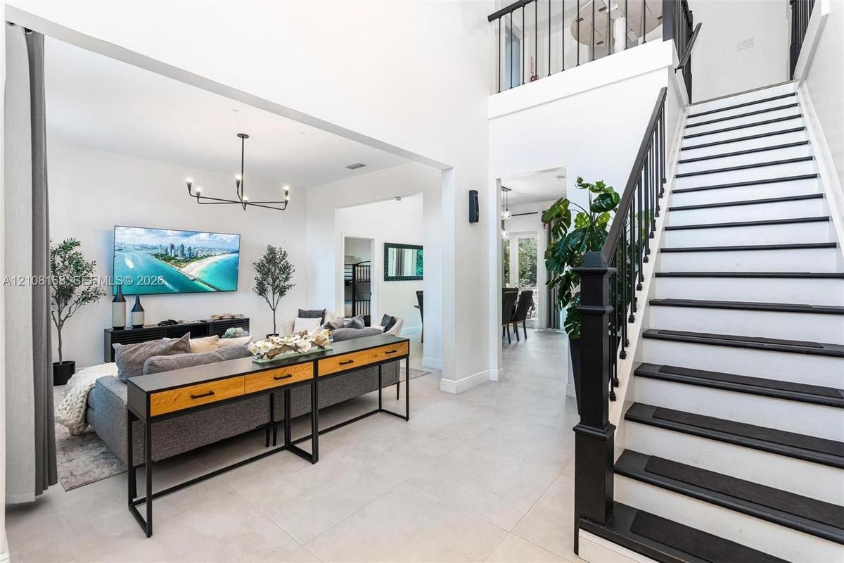 Two-story foyer with high ceilings, large-format tile flooring, a geometric multi-arm chandelier, and a staircase featuring black-painted treads and a