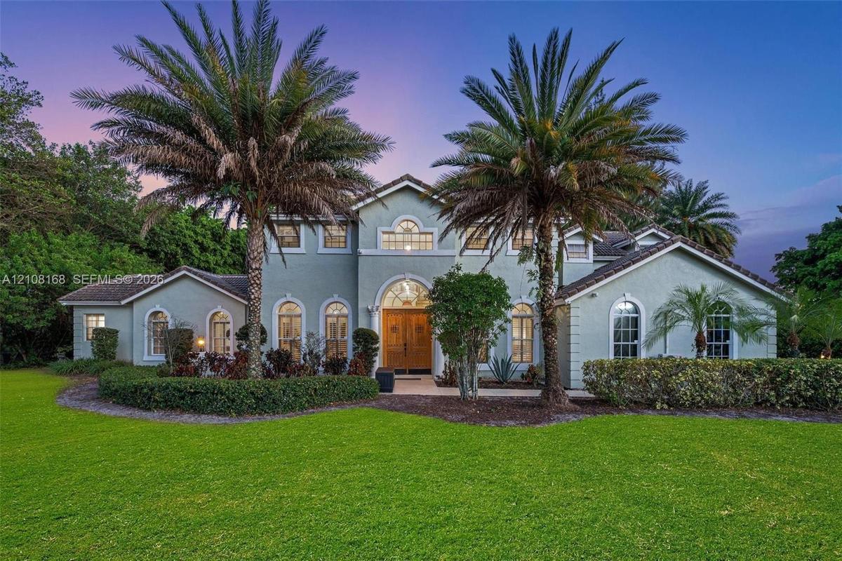 Stucco exterior featuring arched windows, a multi-gabled roofline, double-door entry with arched transom, and mature palm landscaping