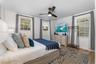 Bedroom featuring wood-finish flooring, three windows with plantation-style shutters, and a central ceiling fan with integrated lighting