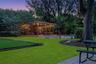 Expansive backyard featuring a covered wood-frame pavilion, manicured lawn, stone paver patio, and mature trees