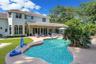 Two-story residence featuring a tile roof, covered rear patio, free-form pool, and manicured landscaping