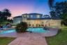 Two-story exterior featuring a hip roof, covered rear patio, freeform swimming pool, integrated spa, and stone-paver hardscaping