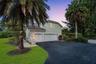 Two-story exterior featuring a stucco facade, tile roof, multi-car garage, asphalt driveway, and mature palm trees