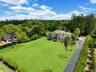 Expansive lot featuring a multi-story residence, extensive lawn area, mature palms, long paved driveway, and perimeter landscaping