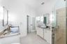 Dual vanity featuring stone countertops, vessel sinks, wall-mounted light fixtures, glass-enclosed shower with tile surround, and frosted glass door