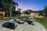 Expansive outdoor living area featuring paved hardscaping, a recessed swimming pool with spa, a wooden pergola, and mature palm trees