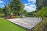 Backyard featuring a sand volleyball court with a boundary frame, a designated play area with wood-chip ground cover, manicured lawn, and mature trees