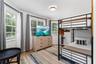 Bedroom featuring wood-finish flooring, three windows with plantation shutters, and a modern ceiling-mounted light fixture