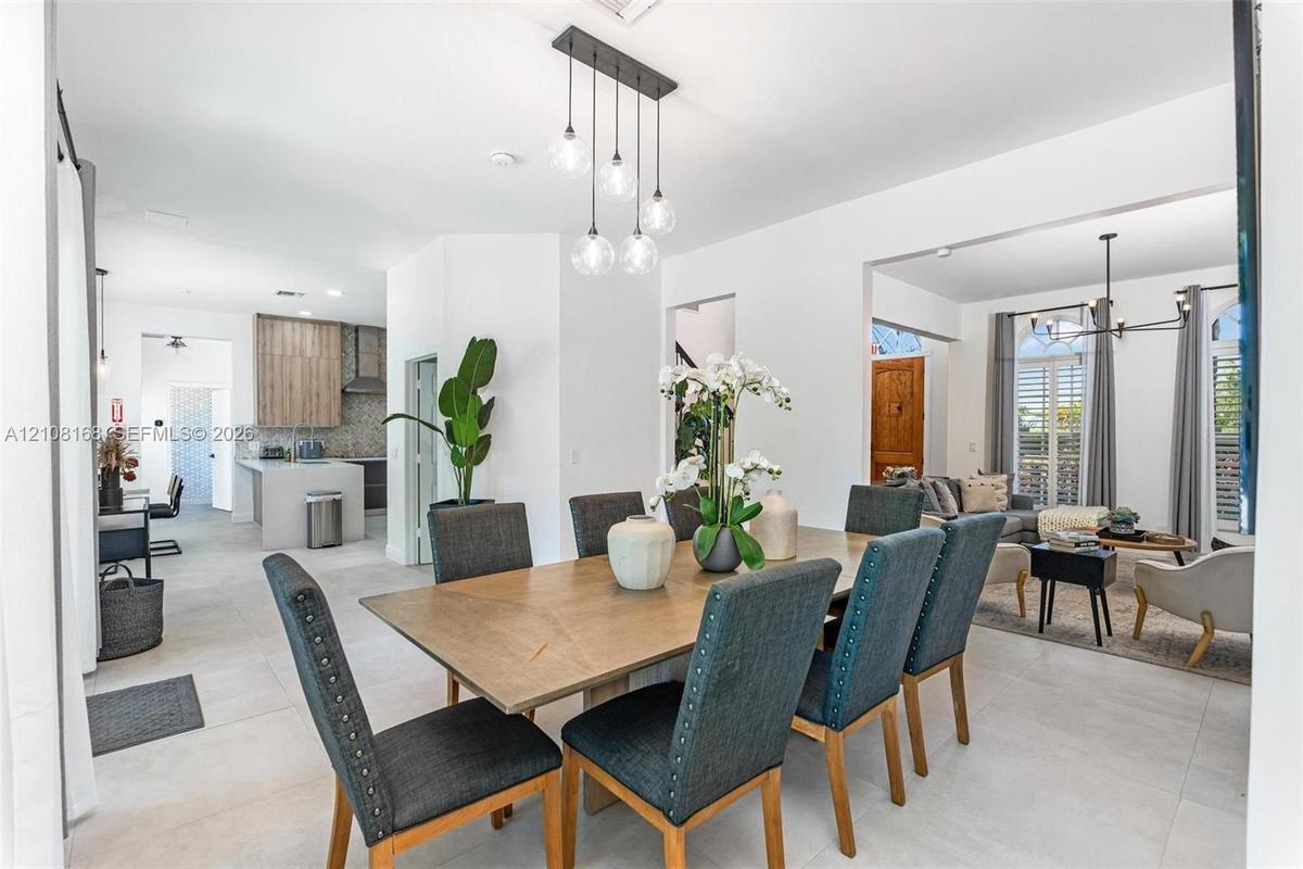 Open-concept interior featuring oversized light-toned floor tiling, a multi-light contemporary pendant fixture, and a minimalist kitchen island with c