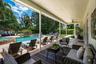 Covered outdoor patio featuring natural stone flooring, a ceiling fan, a swimming pool with rock-style water feature, and a wooden pergola structure