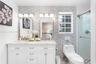 Dual-sink vanity with white cabinetry, patterned tile feature wall, rectangular mirrors, and a glass-enclosed shower