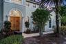 Stucco exterior featuring double arched wood front doors with decorative iron detailing, classical architectural columns, arched windows, and a paved 