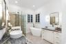 Dual vanities featuring stone countertops and vessel sinks, freestanding soaking tub, glass-enclosed shower with tiled walls, and plantation shutters