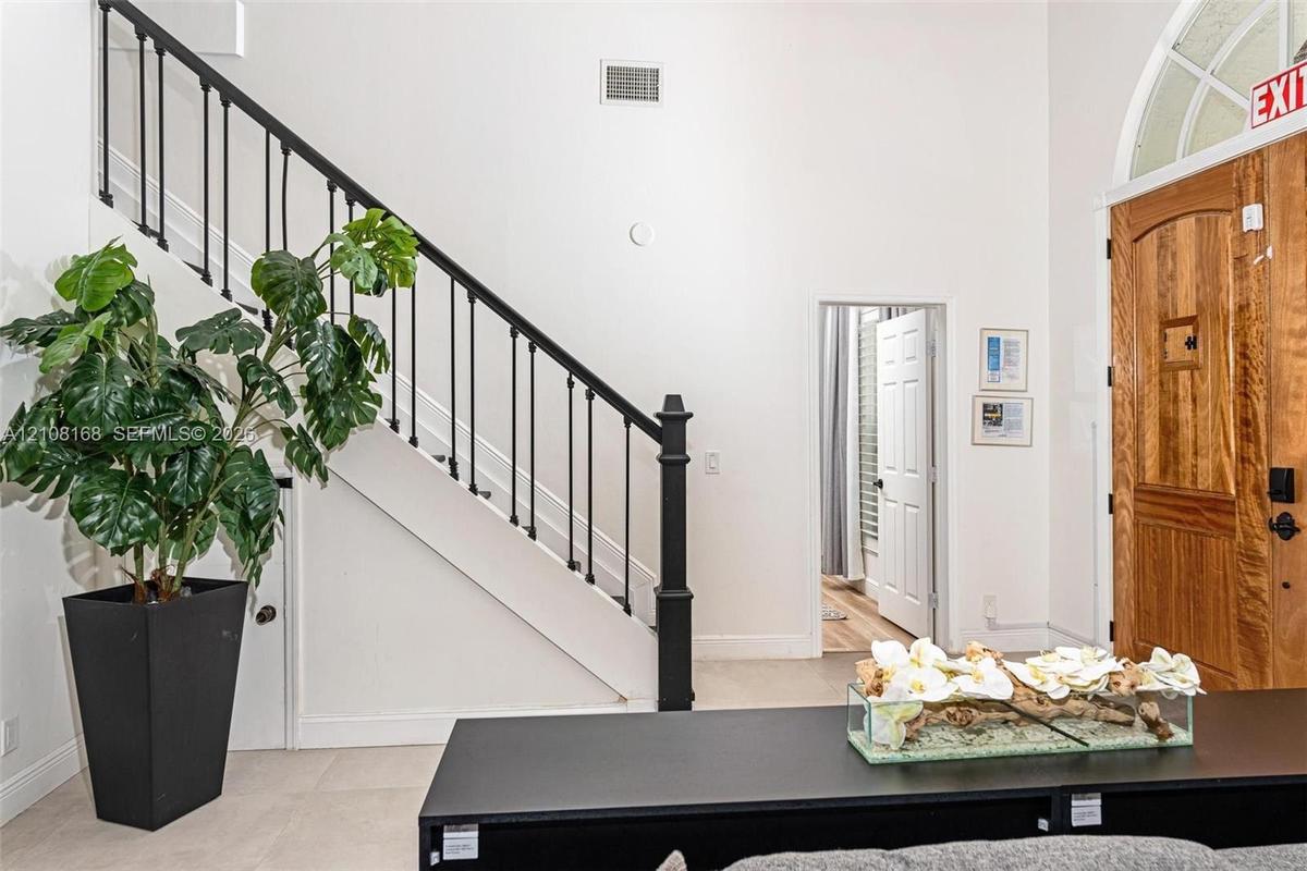 Entryway featuring double-height ceilings, a staircase with black metal balusters, and a wood-paneled door with an arched transom window