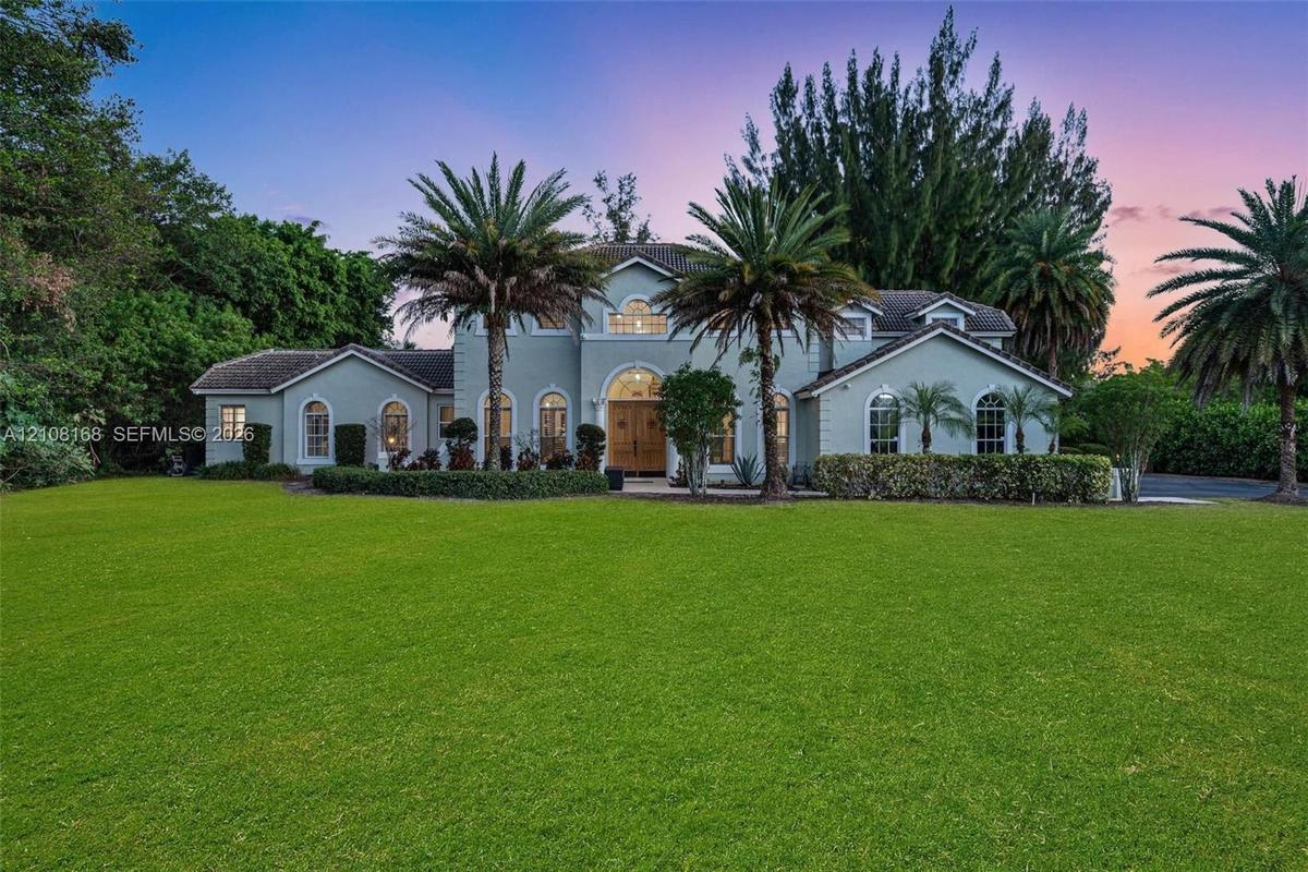 Multi-level residence featuring a stucco exterior, arched window detailing, double entry doors with glass insets, and expansive manicured grounds with