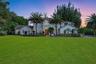 Multi-level residence featuring a stucco exterior, arched window detailing, double entry doors with glass insets, and expansive manicured grounds with