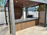 Covered outdoor kitchen featuring horizontal wood slat privacy walls, stone-finish bar top, recessed lighting, and a ceiling-mounted fan, situated on 
