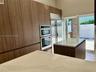 Modern kitchen featuring full-height wood-grain cabinetry, quartz countertops, a dual wall oven, and stainless steel refrigerator