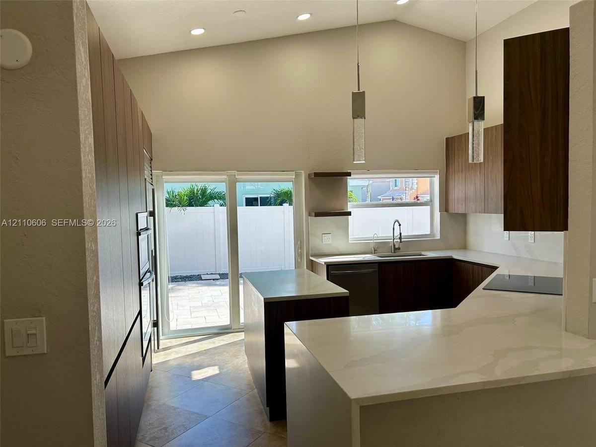 Kitchen featuring flat-panel cabinetry, stone-finish countertops, stainless steel appliances, vaulted ceilings, and pendant lighting