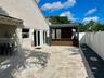 Backyard patio featuring light-toned natural stone pavers, a custom covered outdoor kitchen, wood-slat cabinetry, and solid white perimeter fencing