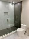 Walk-in shower featuring a frameless glass enclosure, rainfall showerhead, recessed storage niche, and contrast stone-finish tiling, paired with a mod