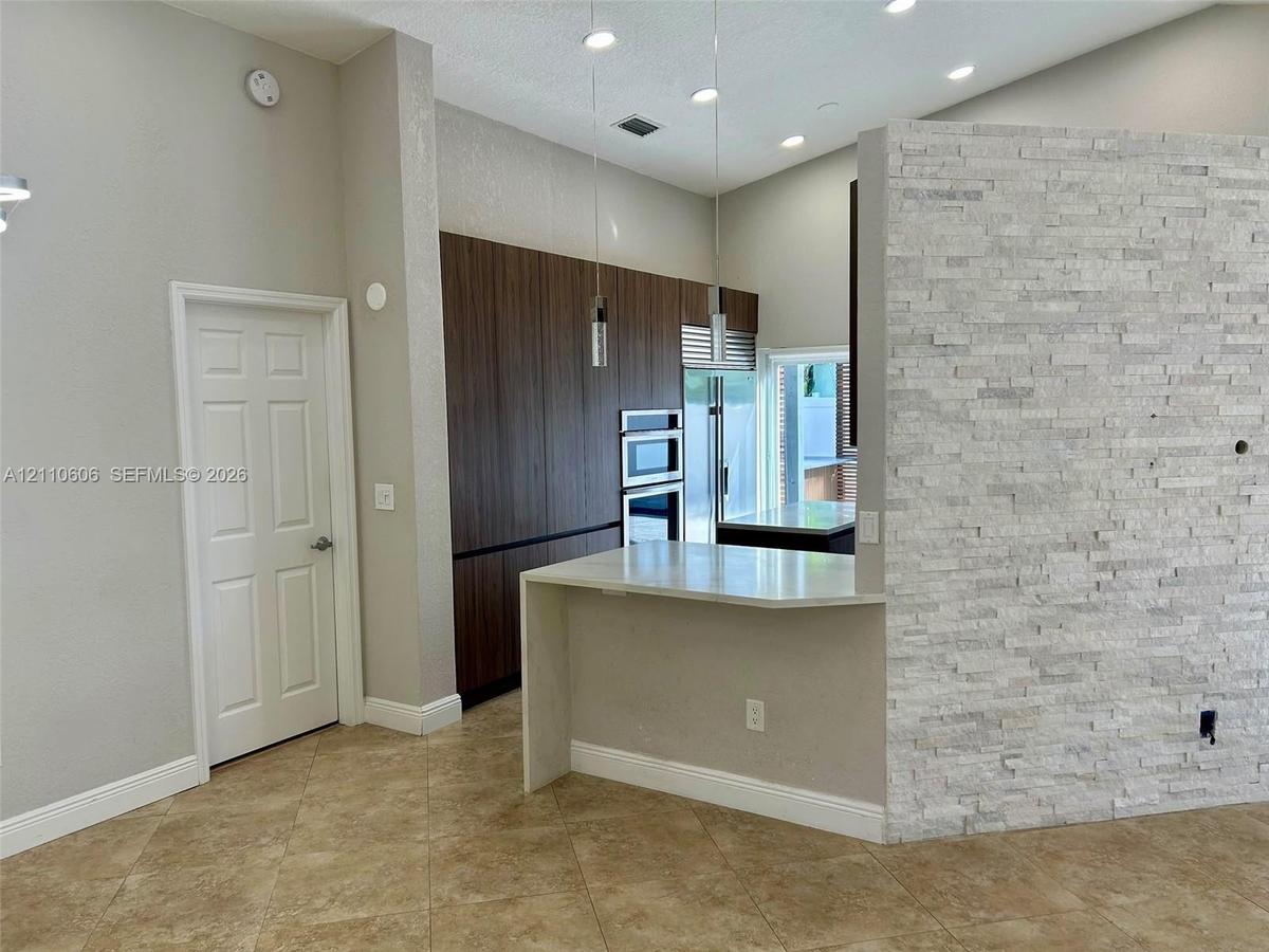 Kitchen featuring flat-panel wood-finish cabinetry, built-in double ovens, a peninsula with a waterfall-edge countertop, and a decorative stone-veneer