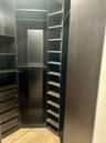 Custom built-in closet organization system featuring dark wood-finish cabinetry, floor-to-ceiling adjustable shelving, multi-tiered hanging rods, and 