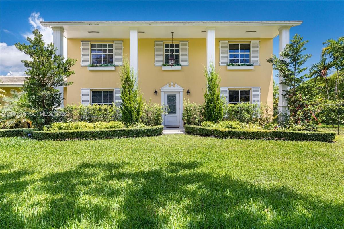 Two-story colonial exterior featuring a covered front porch, prominent structural columns, multi-pane windows with louvered shutters, and window box p