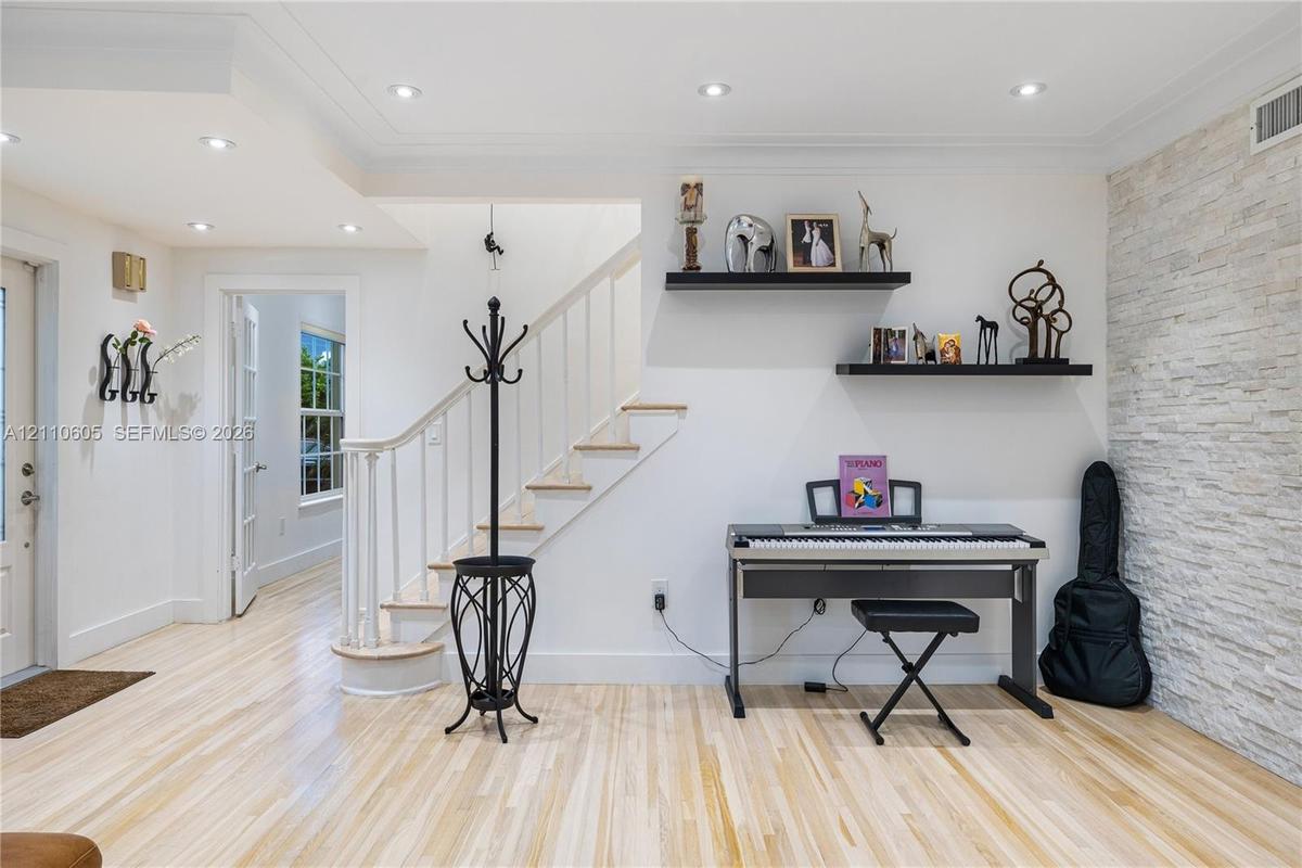 Light wood-finish flooring, textured stone accent wall, recessed lighting, and a staircase with a wooden handrail and balusters