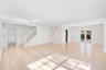 Open-concept interior featuring light wood-finish flooring, recessed lighting, a stone-accented wall, and white staircase railing