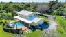 Two-story residence featuring a metal roof, an expansive covered patio, a tiled pool with an integrated spa, and a paved driveway situated on a large,